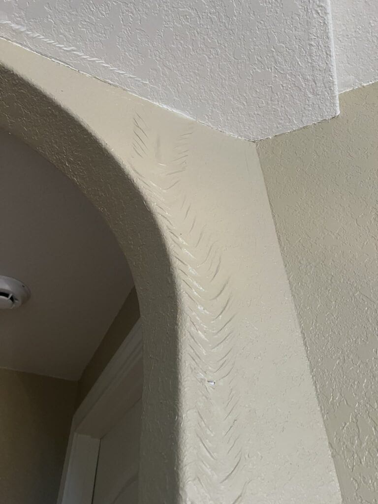 Paint bubbling and wrinkling from moisture damage near archway in Cibolo
